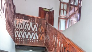 A wooden staircase with intricate railings, a wall-mounted air conditioning unit, and a fire hose reel. - The Hub Train House Exotic Roots (Zanzibar)