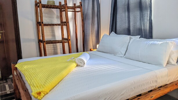 A bed with white bedding, a yellow blanket, and a rolled towel. - The Hub Train House Exotic Roots (Zanzibar)