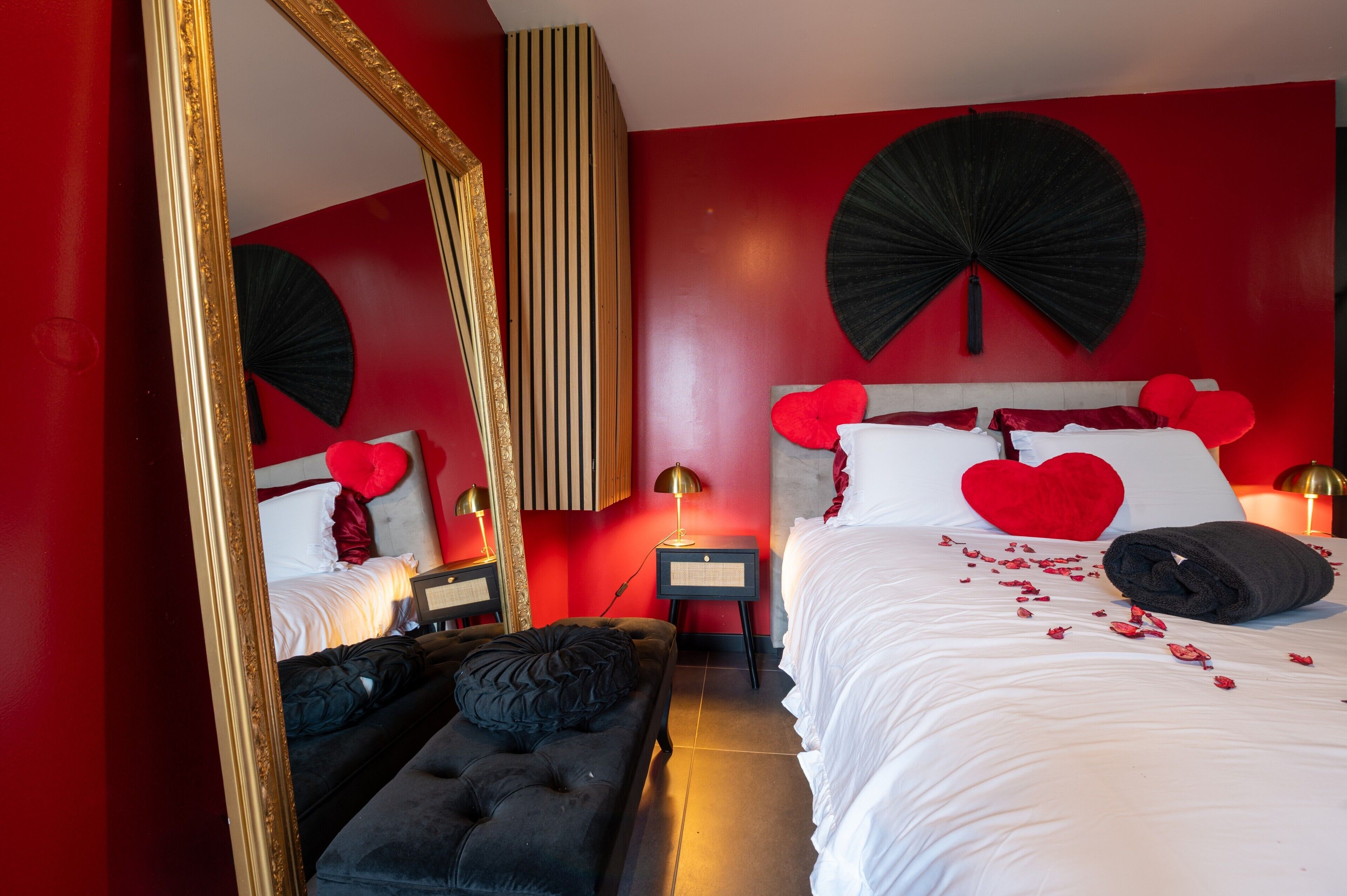 Een slaapkamer met een groot bed, een spiegel, een nachtkastje en een rode wand.