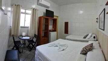 Quarto de hotel com duas camas, uma mesa pequena com cadeiras, ar condicionado e uma janela com cortinas.