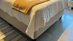 Ein ordentlich bezogenes Bett mit einer gepolsterten Kopfteil, einer Lampe und Blick ins Freie durch ein großes Fenster.