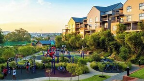 Ein Spielplatz mit verschiedenen Spielgeräten, umgeben von gepflegtem Rasen und Wegen.