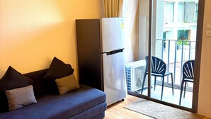 Un salon comprenant un canapé, un réfrigérateur et une porte-fenêtre coulissante donnant sur un espace extérieur aménagé avec des chaises.