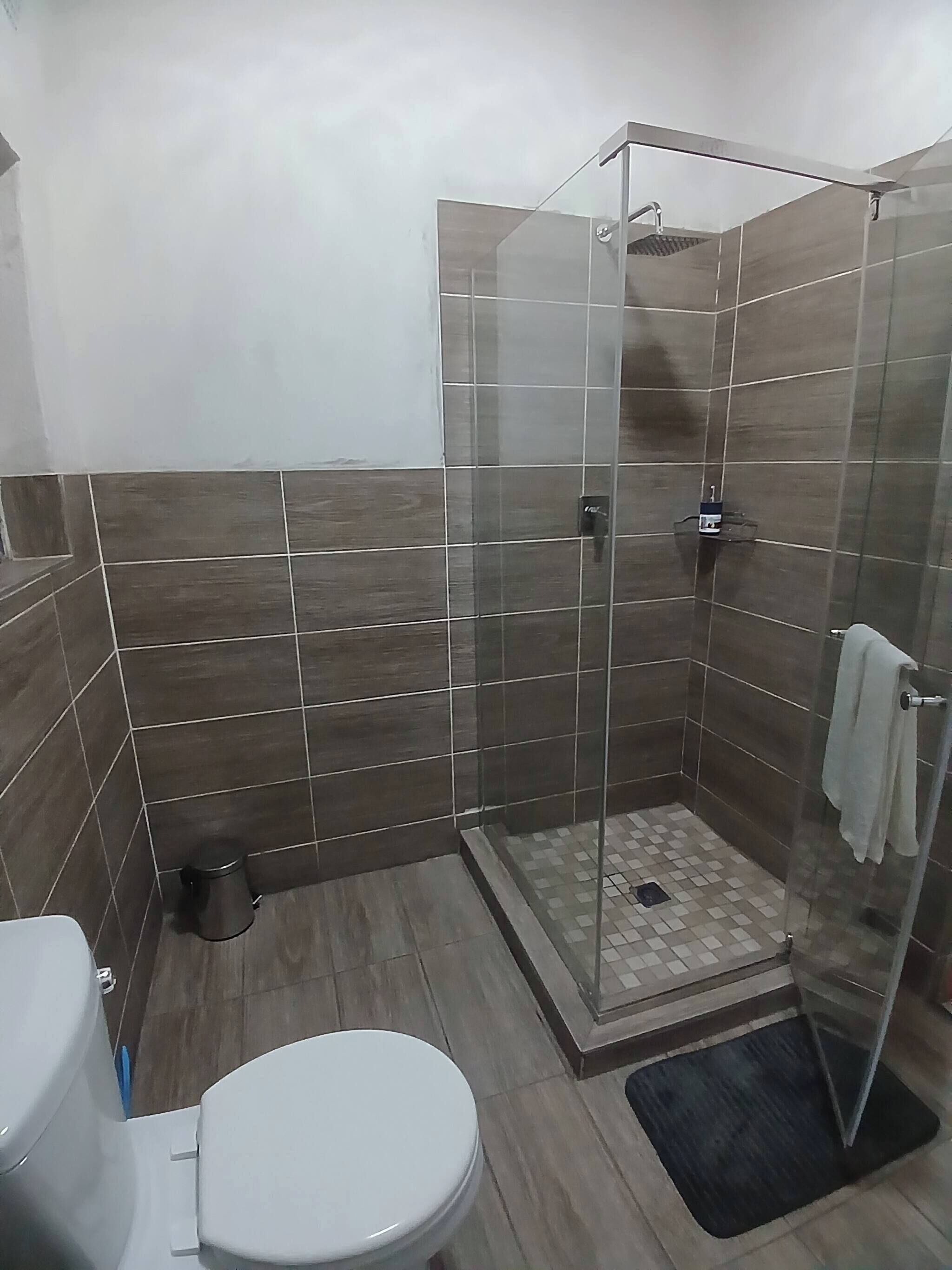 Et badeværelse med toilet, bruser med glasdør og flisebeklædte vægge.