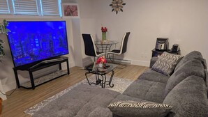 En stue med sofa, sofabord, fjernsyn og et spiseområde med stole samt en vase med blomster.