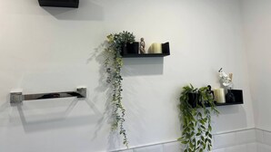 A bathroom with white walls, a towel rack, and three black shelves with plants and decorative items. - Salvation View 2 Bed Apartment (Hadleigh)