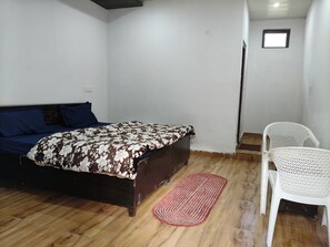 Une chambre à coucher avec un lit, une chaise, une petite fenêtre et un plancher en bois.