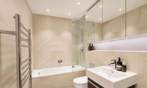 Ein modernes Badezimmer mit Duschkabine aus Glas, einer weißen Badewanne und einem Waschtisch mit Waschbecken und Spiegel.