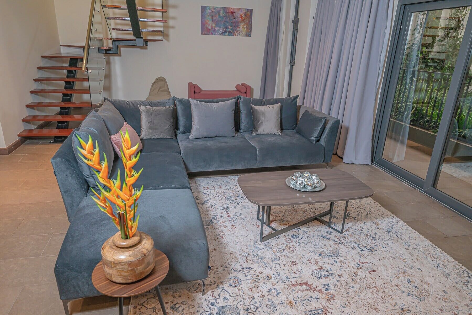 Uma sala de estar moderna com um sofá modular cinza, uma mesa de centro de madeira e uma escada com guarda-corrimão de vidro.