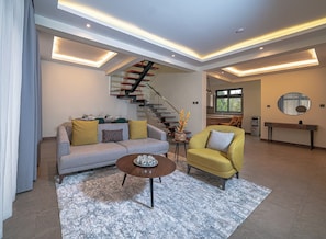 Ein modernes Wohnzimmer mit Sofa, Sessel, Couchtisch und einer Treppe.