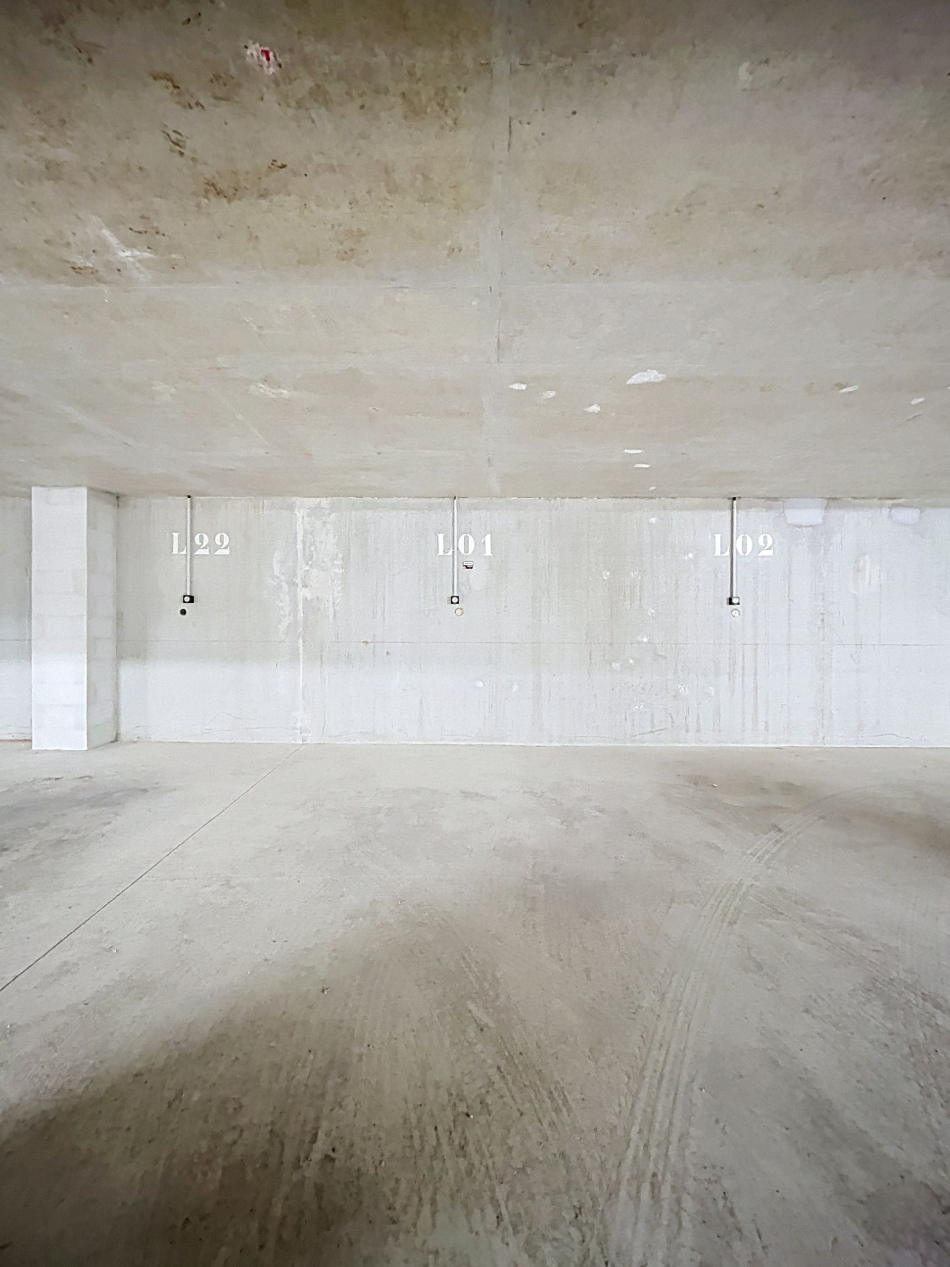 Une pièce vide avec un sol et des murs en béton, portant les numéros L01, L02 et L22.