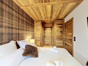 A hotel room with a large bed, wooden ceiling, and a plaid-patterned wall. - The Douka Apartment—Sleeps 4—Near Downtown (Les Gets)