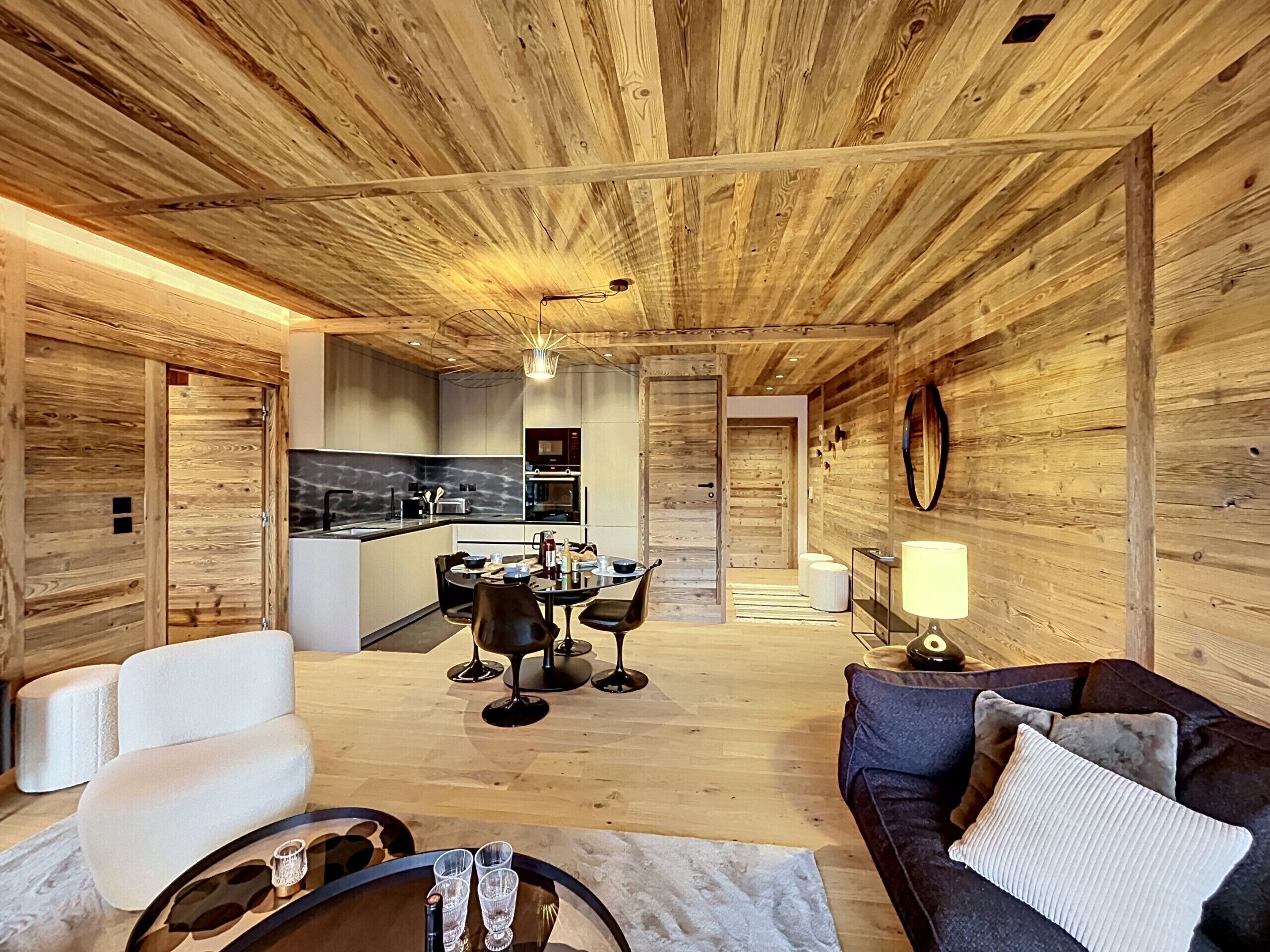 A spacious living area with a wooden ceiling, a dining table with chairs, a sofa, and a coffee table.