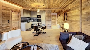En rummelig opholdsstue med træloft, spisebord med stole, sofa og sofabord.