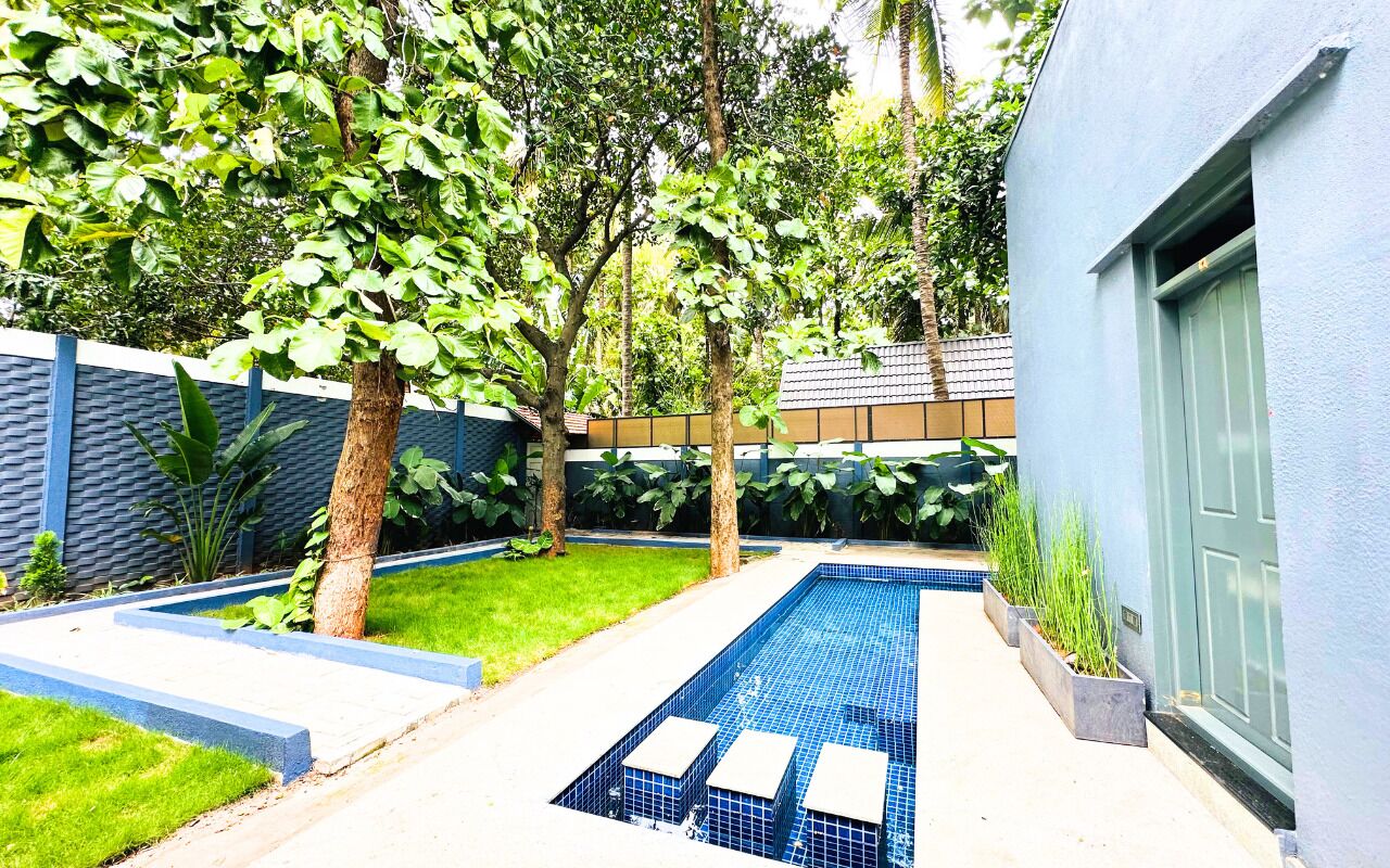 A modern outdoor pool area with a blue tiled pool, surrounded by trees and a low wall.