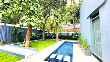 A modern outdoor pool area with a blue tiled pool, surrounded by trees and a low wall.