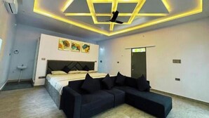 Une chambre moderne avec un lit, un canapé, un ventilateur de plafond et des œuvres d’art accrochées au mur.