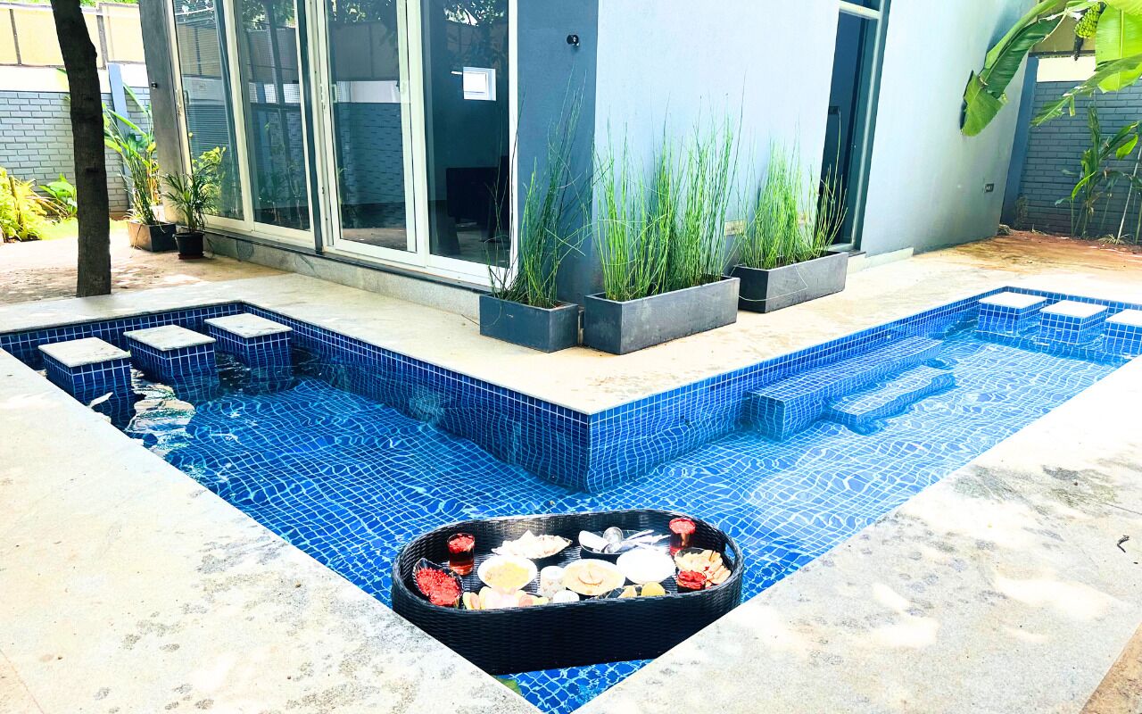 Uma piscina com azulejos de mosaico azul, uma banheira de hidromassagem e plantas em vasos.