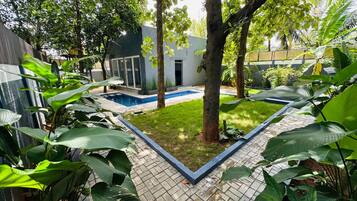 A modern house with a swimming pool, surrounded by lush greenery and a paved patio.