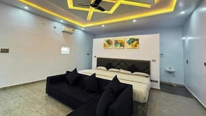 Une chambre à coucher avec un lit, un canapé noir, un ventilateur de plafond, un éclairage encastré et des œuvres d’art accrochées au mur.