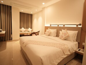 Habitación de hotel con una cama grande, una mesita de noche, una silla, una pequeña mesa y un espejo.