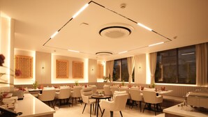 Une chambre d’hôtel moderne dotée d’un coin repas, d’un comptoir de réception et d’une grande fenêtre avec des rideaux.