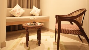 Un salon accueillant avec un canapé, un fauteuil en bois et une petite table ronde sur laquelle se trouve un plateau de collations.