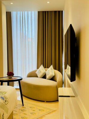 A modern hotel room with a curved sofa, a flat-screen TV mounted on the wall, and a small table with a vase of flowers. - HARI VILAAS KASHI (Varanasi)
