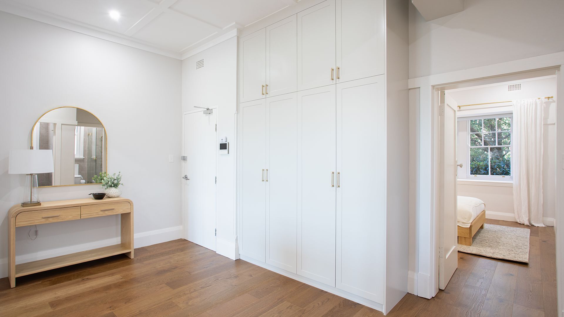 Une pièce avec une coiffeuse en bois, une grande armoire blanche et une fenêtre donnant sur un paysage verdoyant.