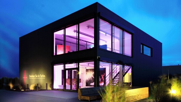 A modern building with large glass windows, a staircase, and a bench outside.