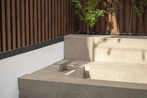 Eine Betonbank mit Metallgestell, ein Holzzaun und eine kleine Pflanze in einer Gartenanlage.