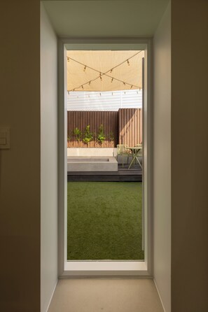 A view through a window into a room with a green artificial turf, a wooden deck, and a string of lights.