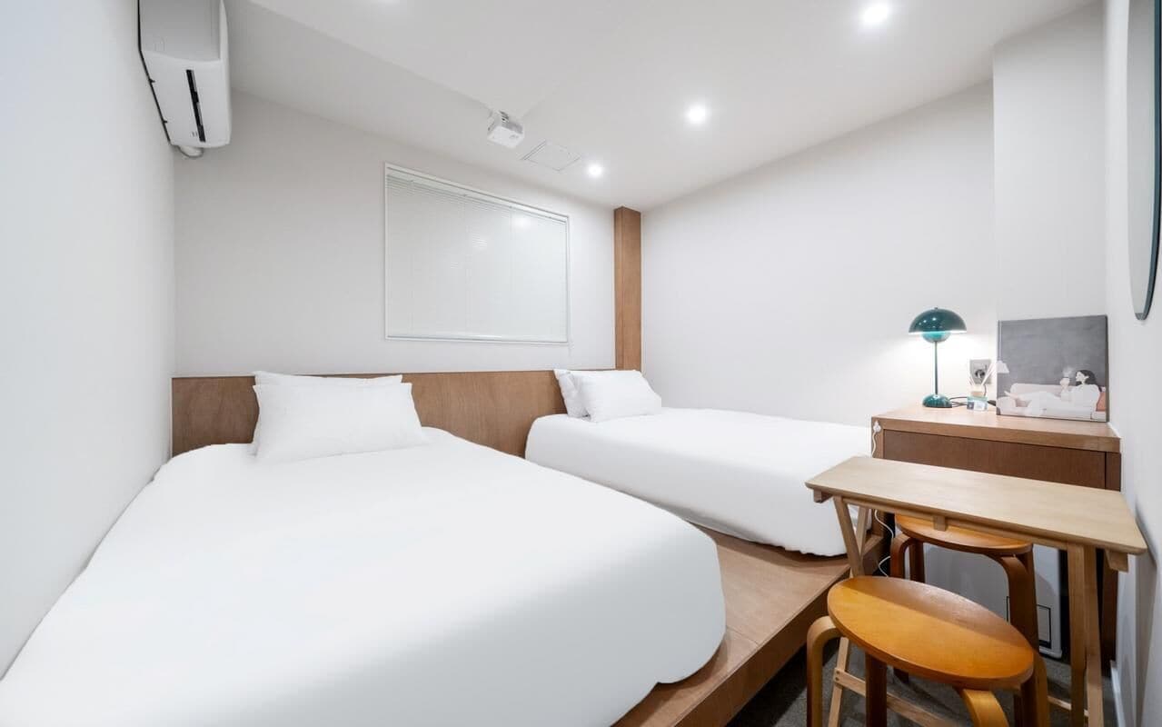 A hotel room with two beds, a desk, a chair, a lamp, and a small table.