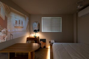 A hotel room with a bed, a desk, a chair, a lamp, a window with blinds, and a wall-mounted projector screen displaying a movie scene. - Lua Hotel (Seoul)