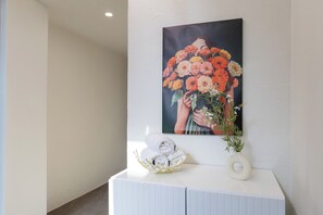 A white console table with a painting of flowers, a rolled towel, and a vase with a plant.