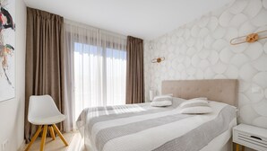 Une chambre à coucher comprenant un lit, une chaise, une table de chevet et un mur orné d’un motif géométrique.