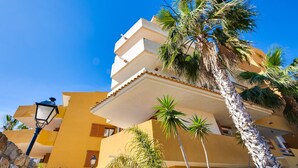 Un immeuble à plusieurs étages doté de balcons, de palmiers et surplombant un ciel d’un bleu limpide.