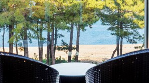 Blick auf einen Strand mit Kiefern und einem Tisch mit Stühlen im Vordergrund.
