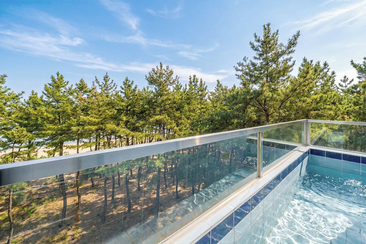 Una piscina infinita con paredes de vidrio y vistas a un área boscosa.