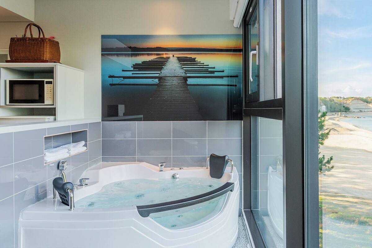 Un baño moderno con una bañera grande, un microondas y una cesta de mimbre en un estante.