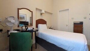 Hotellihuone, jossa on sänky, tuulettimella varustettu työpöytä, tuoli, peili, seinään kiinnitetty valaisin ja ovi.