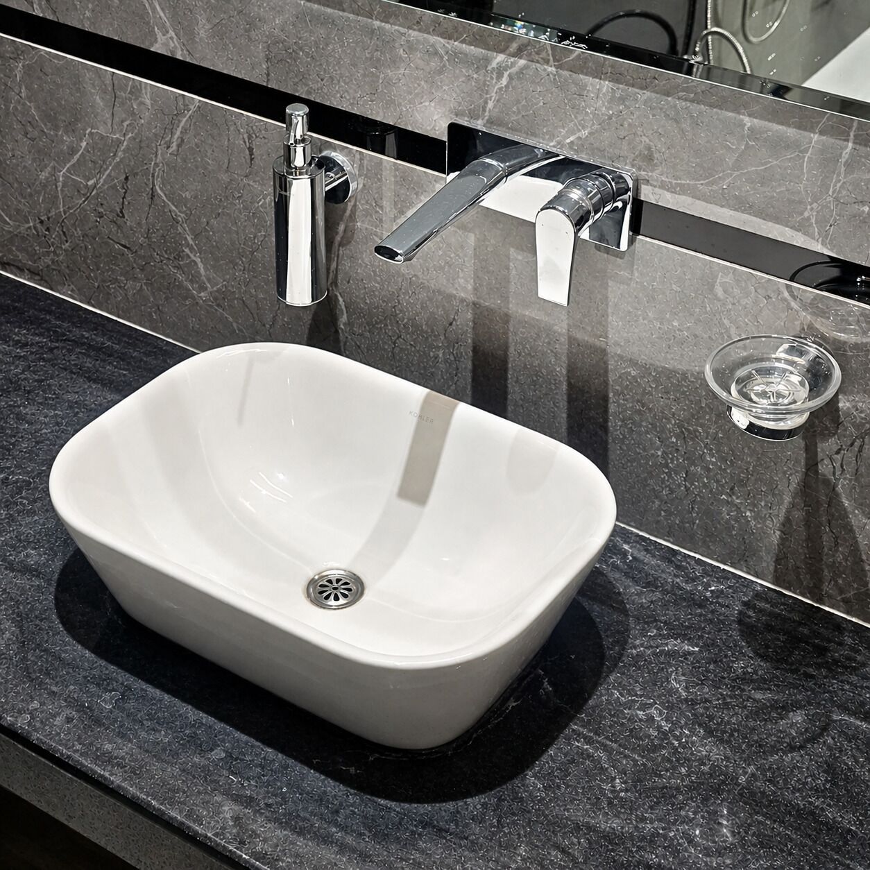 A bathroom with a white vessel sink, a mirror, and a black marble countertop.