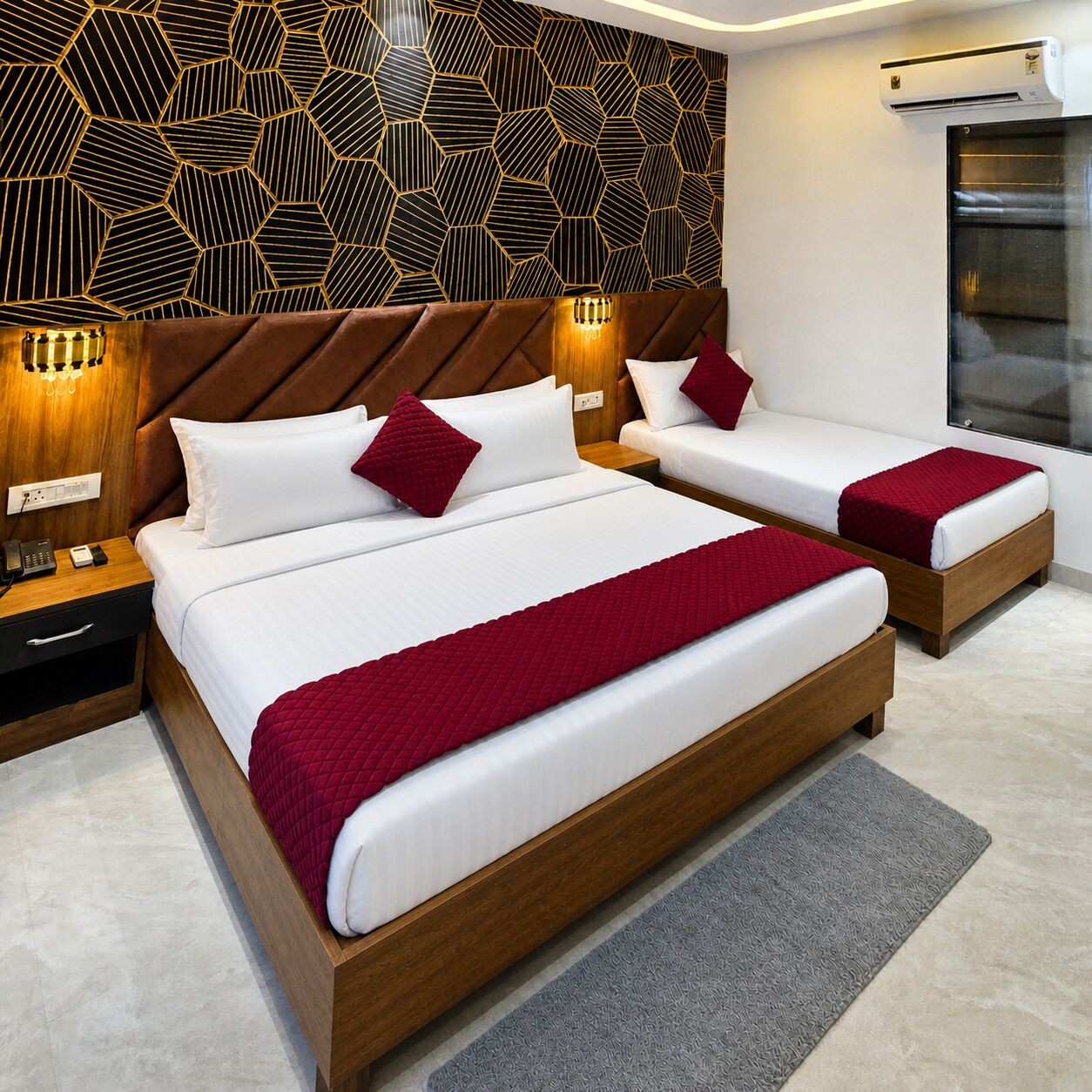 Habitación de hotel con dos camas, un revestimiento mural de estampado geométrico, un cabecero moderno, lámparas de noche, un equipo de aire acondicionado integrado y una mesita de noche pequeña con un teléfono.