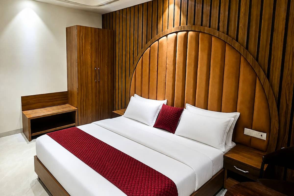 A modern bedroom with a wooden headboard, a large bed with white and red bedding, a wooden nightstand, and a wooden wardrobe.