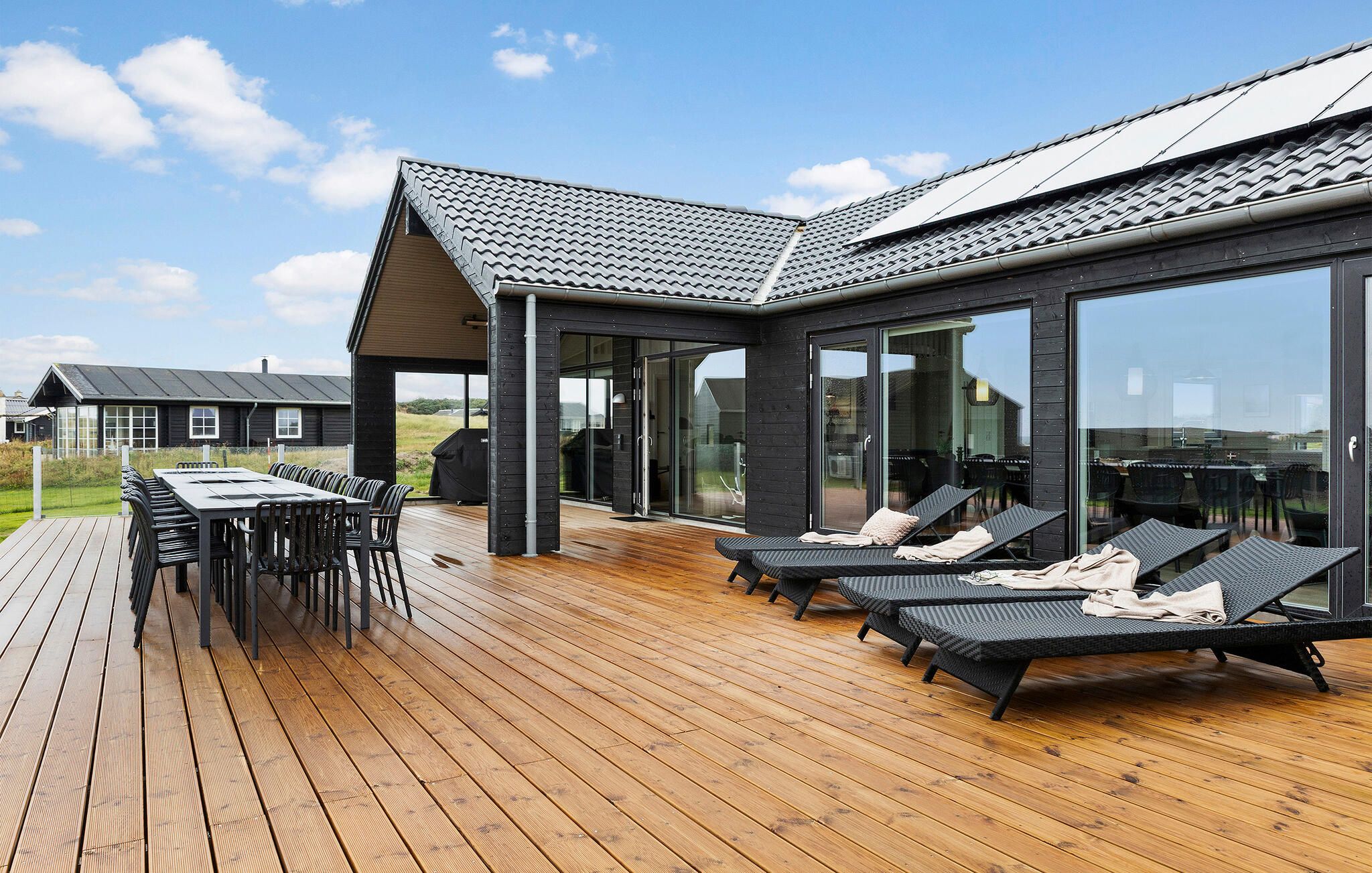 Une terrasse extérieure moderne avec un plancher en bois, un espace repas avec des chaises et des fauteuils de détente avec des coussins.