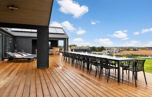 Una terraza al aire libre con una mesa larga y sillas, una parrilla y una zona de estar cubierta con sillones reclinables.