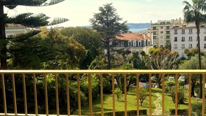 Un balcón con barandilla amarilla que da a un jardín cuidado y vistas de edificios a lo lejos.