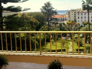 Ein Balkon mit gelbener Geländer, der auf einen gepflegten Garten und eine Fernsicht auf Gebäude blickt.