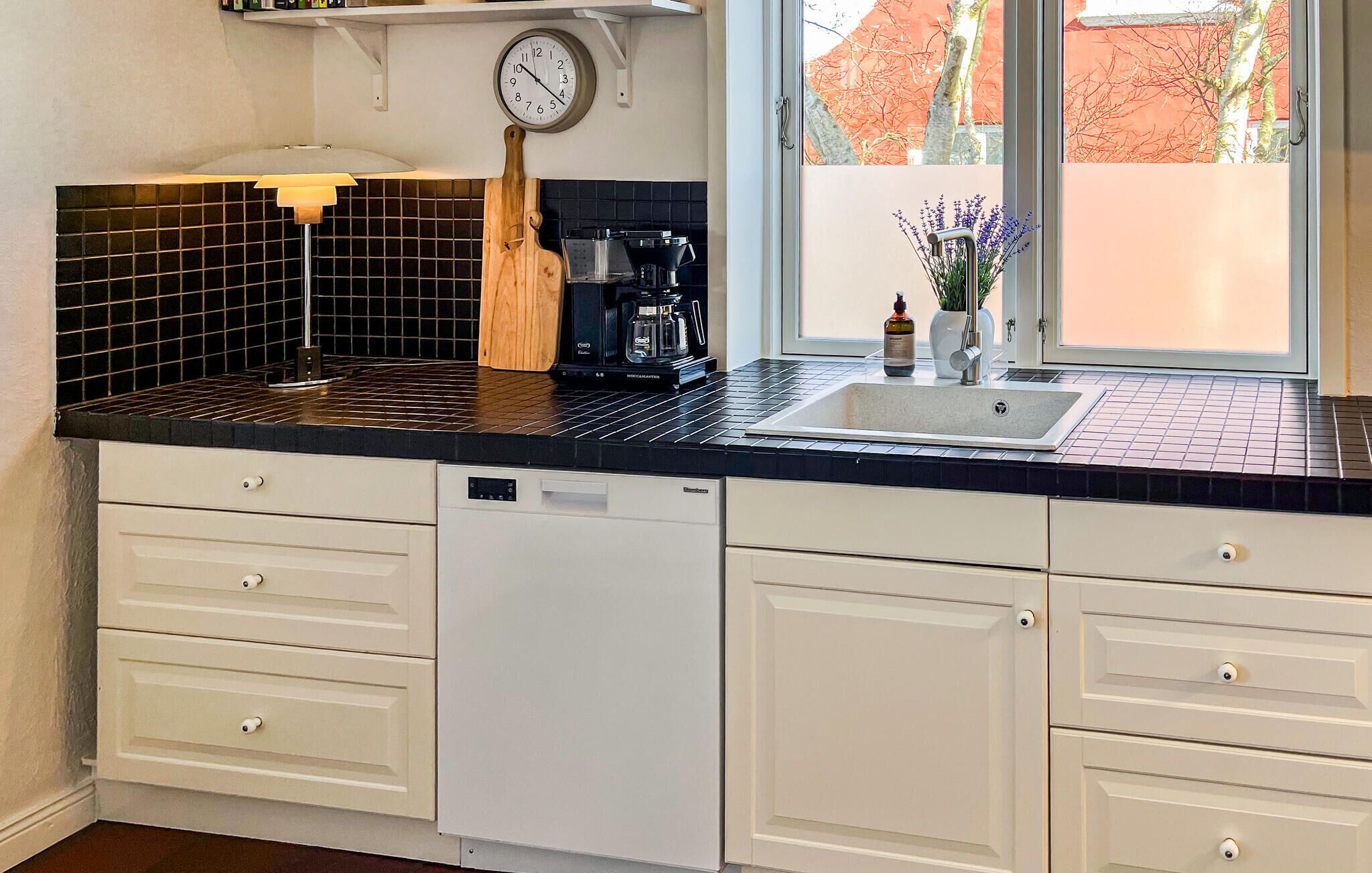 A kitchen with a black countertop, white cabinets, a coffee maker, and a clock.