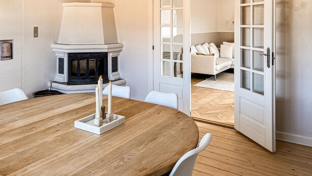 A round wooden table with a white candle holder, a fireplace, and a white door leading to a living area. - Beautiful home in Saltum with WiFi (Saltum)